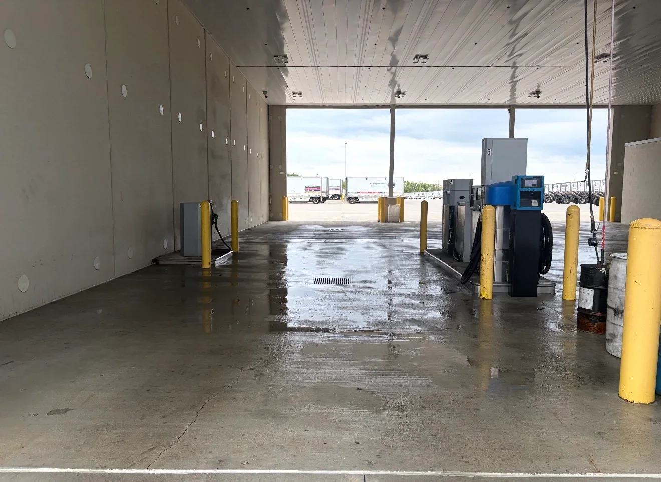 Wet concrete loading dock floor after pressure washing, yellow safety bollards, industrial bay