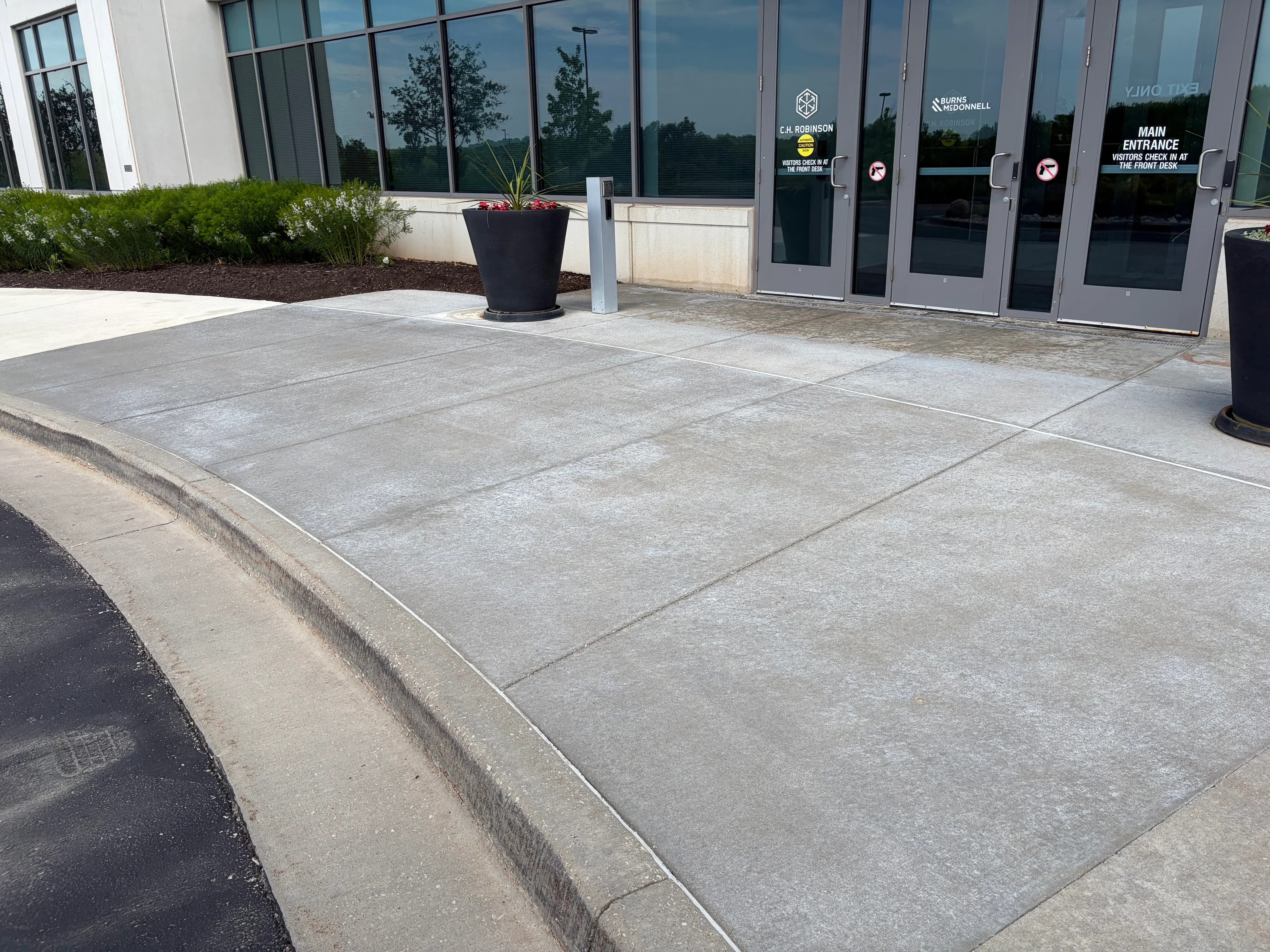 Clean gray concrete paver entrance with grout lines, commercial building facade with glass doors
