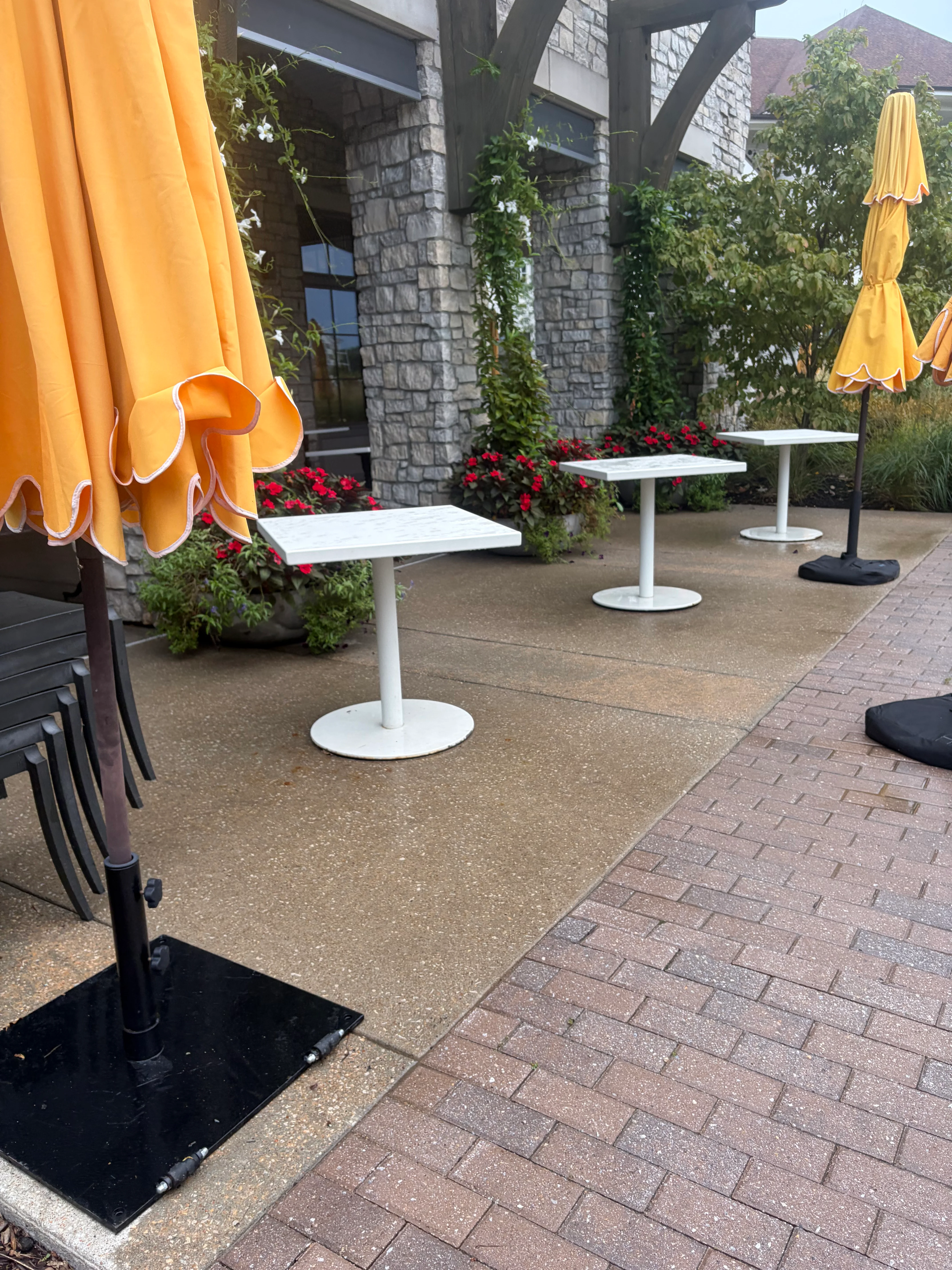 Clean concrete and brick paver patio with white tables and yellow umbrellas